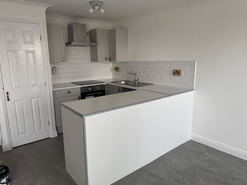 A fitted kitchen with grey units and a white tiled splashback