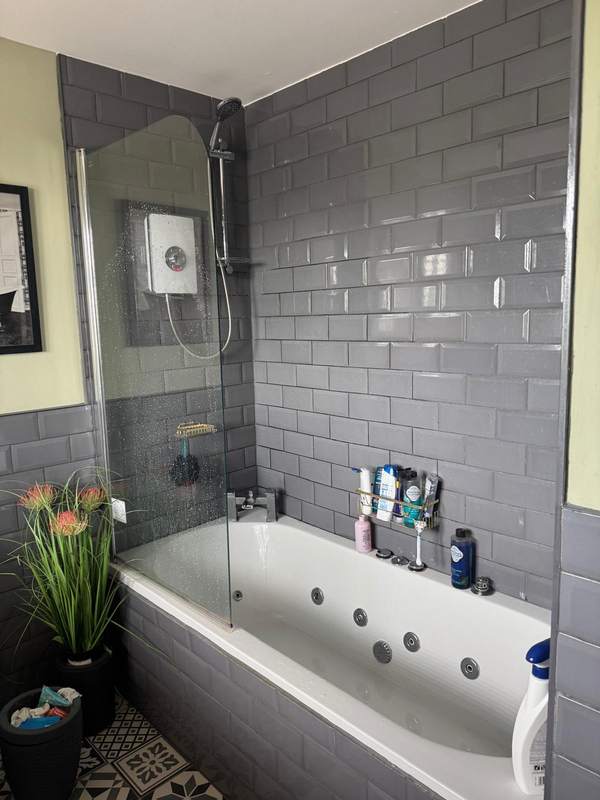 A fitted bathroom with grey wall tiles and a shower screen over the bath
